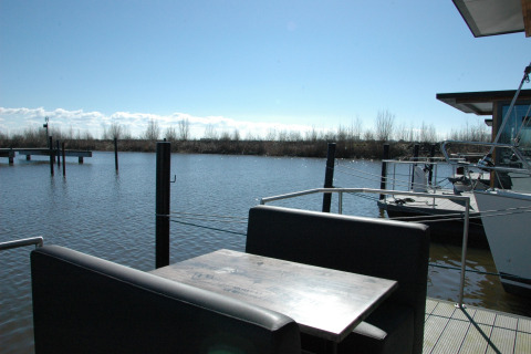 View from houseboat named 'Boat' in the Netherlands with table, benches, water and natural scenery.