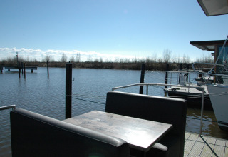 View from houseboat named 'Boat' in the Netherlands with table, benches, water and natural scenery.