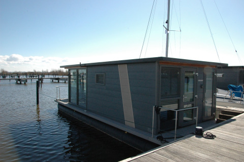 Modern houseboat docked at a pier, photo taken at Boat No Name, with calm water and clear sky.