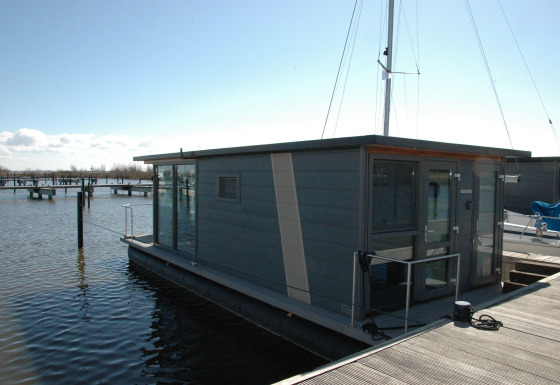 Modern houseboat docked at a pier, photo taken at Boat No Name, with calm water and clear sky.