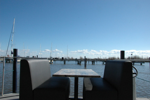 View from a houseboat in the Netherlands showing a table with benches by the marina and blue sky.