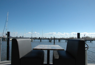 View from a houseboat in the Netherlands showing a table with benches by the marina and blue sky.