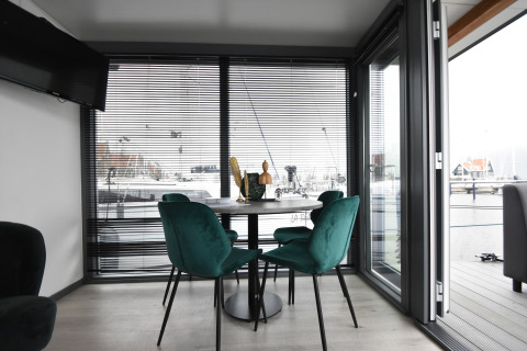 Modern dining area with green chairs aboard houseboat 'Boat' in the Netherlands with marina view.