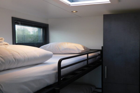 Bright modern bedroom with bunk bed, white bedding, wardrobe, and window inside a Dutch houseboat.