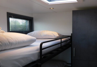 Bright modern bedroom with bunk bed, white bedding, wardrobe, and window inside a Dutch houseboat.