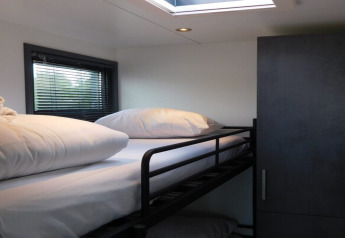 Bright modern bedroom with bunk bed, white bedding, wardrobe, and window inside a Dutch houseboat.