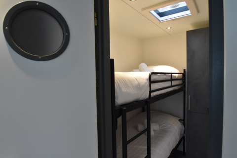 A bedroom with bunk beds and a skylight on a houseboat in the Netherlands, viewed through a door.
