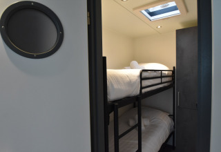 A bedroom with bunk beds and a skylight on a houseboat in the Netherlands, viewed through a door.