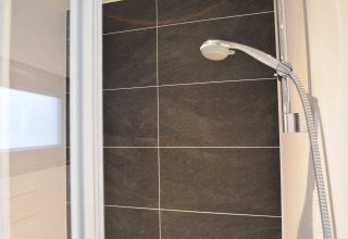 Modern shower with dark tiles and handheld shower head in a houseboat named "Boat" in the Netherlands.