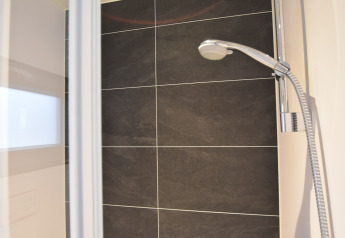 Modern shower with dark tiles and handheld shower head in a houseboat named "Boat" in the Netherlands.