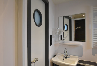 Bathroom on houseboat 'Boat' in the Netherlands, with round window door, mirror, and sink.