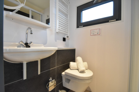 Modern bathroom on a houseboat in the Netherlands with sink, toilet, window, and rolled towels.