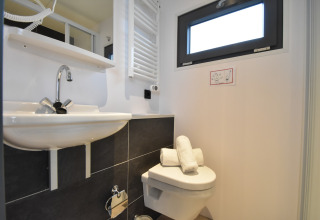Modern bathroom on a houseboat in the Netherlands with sink, toilet, window, and rolled towels.