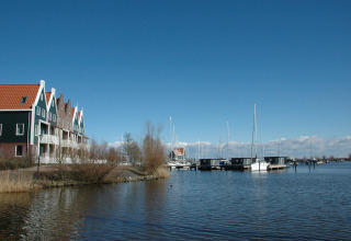 Panorama of a canal with a houseboat named 'Boat', yachts, and Dutch houses under a clear blue sky.
