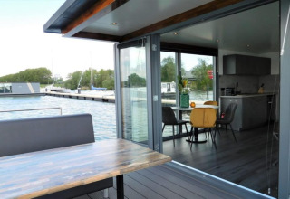 Modern houseboat in the Netherlands with open interior, dining area, and waterside terrace view.