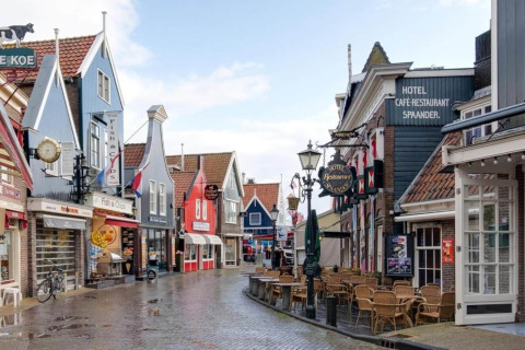 Colorful Dutch street with distinctive facades, cafes, and empty outdoor seating on a wet day.