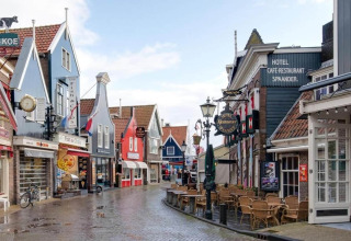 Colorful Dutch street with distinctive facades, cafes, and empty outdoor seating on a wet day.