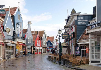 Colorful Dutch street with distinctive facades, cafes, and empty outdoor seating on a wet day.