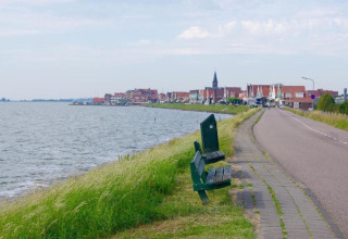View from a houseboat in the Netherlands featuring a bench by the water and a village in the distance.