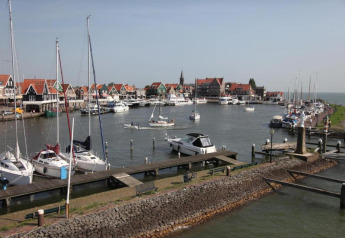 View of a harbor with sailboats and colorful houses by the water in the Netherlands, taken from a houseboat.