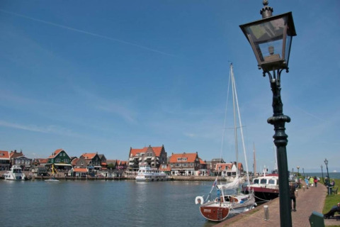 Houseboat named 'Boat' docked in a Dutch village, with colorful houses and boats along the waterfront.
