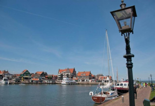 Houseboat named 'Boat' docked in a Dutch village, with colorful houses and boats along the waterfront.