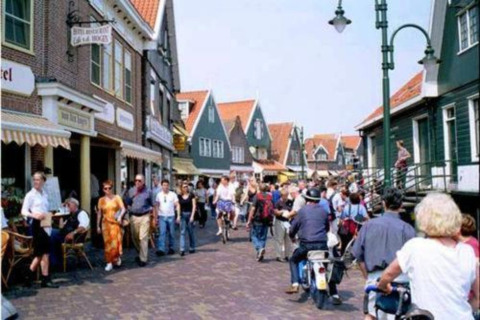 Busy Dutch street scene with people walking, cycling, and riding scooters past traditional houses.