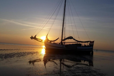 Houseboat named «Boat» during sunset in the Netherlands, resting on shallow water with a clear reflection.