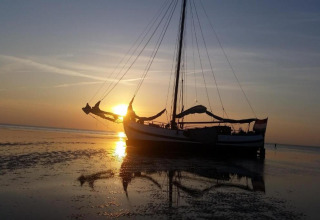 Houseboat named «Boat» during sunset in the Netherlands, resting on shallow water with a clear reflection.