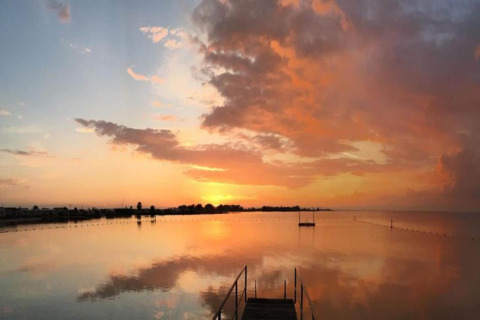 Sunset over calm water at a houseboat named «Boat» in the Netherlands, with vibrant clouds and peaceful reflection.