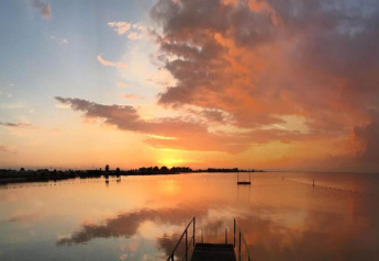 Sunset over calm water at a houseboat named «Boat» in the Netherlands, with vibrant clouds and peaceful reflection.