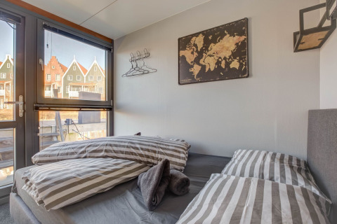 Camera da letto su una casa galleggiante a Volendam con biancheria a righe, mappa e vista su case colorate.