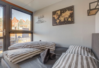 Soveværelse på husbåd i Volendam med stribet sengetøj, vægkort og vindue med udsigt over farverige huse.