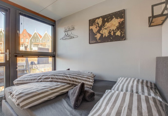 Camera da letto su una casa galleggiante a Volendam con biancheria a righe, mappa e vista su case colorate.