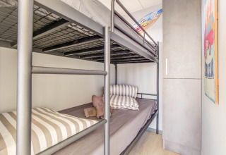 Habitación con literas, cojines a rayas, armario y tabla de surf en una casa flotante en Volendam, Países Bajos.