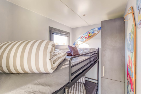 Moderne stapelbedkamer op een woonboot in Volendam, Nederland, met surfplank en gestreept beddengoed.
