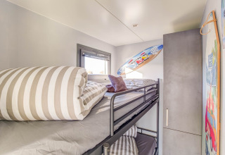 Habitación moderna con literas en una casa flotante en Volendam, Países Bajos, con tabla de surf y ropa de cama rayada.