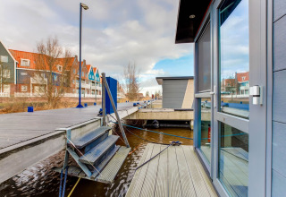 Zicht vanaf een woonboot in Volendam bij Fort Edam, Nederland, met steiger en kleurrijke huizen aan het water.