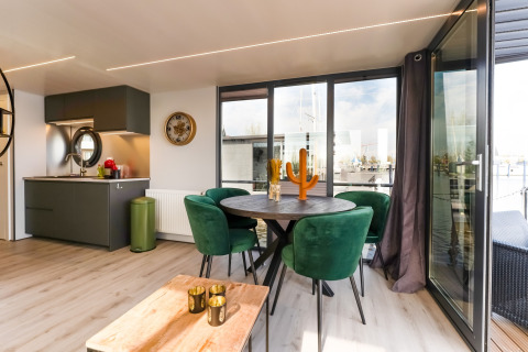 Soggiorno e cucina moderni sulla houseboat La Belle Vie nei Paesi Bassi con sedie verdi e ampie finestre.