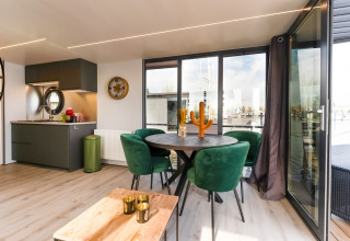 Soggiorno e cucina moderni sulla houseboat La Belle Vie nei Paesi Bassi con sedie verdi e ampie finestre.