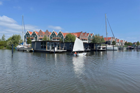 Husbåde og sejlbåde i Volendam nær Fort Edam, Holland, med farverige huse i baggrunden.
