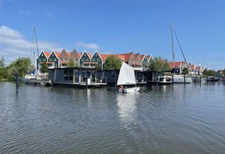 Casa flotante y veleros en Volendam cerca de Fort Edam, Países Bajos, con casas coloridas al fondo.