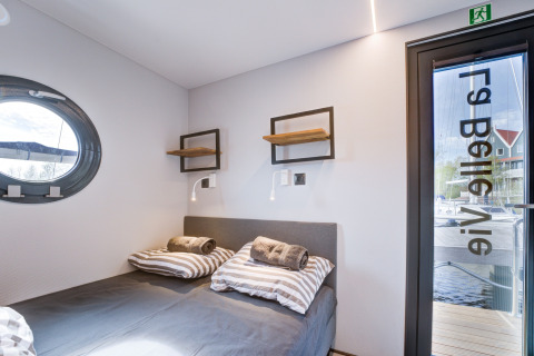 Camera moderna sulla houseboat La Belle Vie nei Paesi Bassi con oblò, letto matrimoniale e vista esterna.