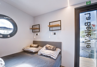 Camera moderna sulla houseboat La Belle Vie nei Paesi Bassi con oblò, letto matrimoniale e vista esterna.