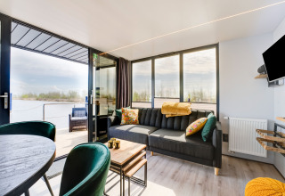 Soggiorno sulla houseboat 'La Belle Vie' in Olanda, arredamento moderno, grandi finestre e vista sull’acqua.