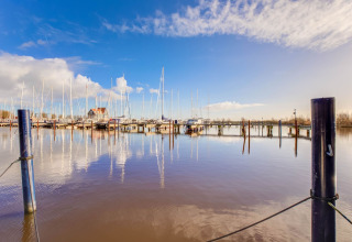 Udsigt over en rolig havn med sejlbåde og husbåde i Volendam nær Fort Edam under en blå himmel.
