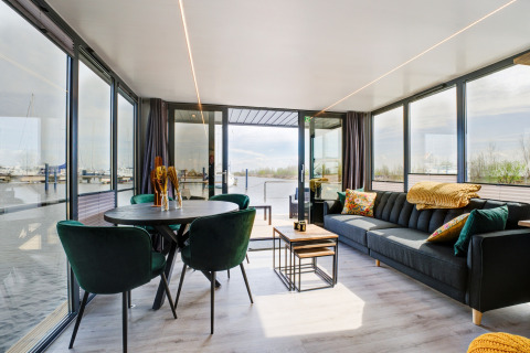 Soggiorno moderno sulla houseboat La Belle Vie nei Paesi Bassi, con grandi finestre e vista sul porto.