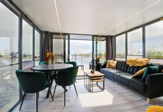 Soggiorno moderno sulla houseboat La Belle Vie nei Paesi Bassi, con grandi finestre e vista sul porto.