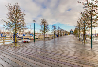 Holzsteg mit Bäumen und Bootshafen in Volendam bei Fort Edam, Niederlande, an einem wolkigen Tag.