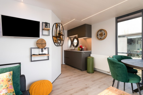Interno di una moderna houseboat con soggiorno, piccola cucina, decorazioni e sedie verdi nei Paesi Bassi.